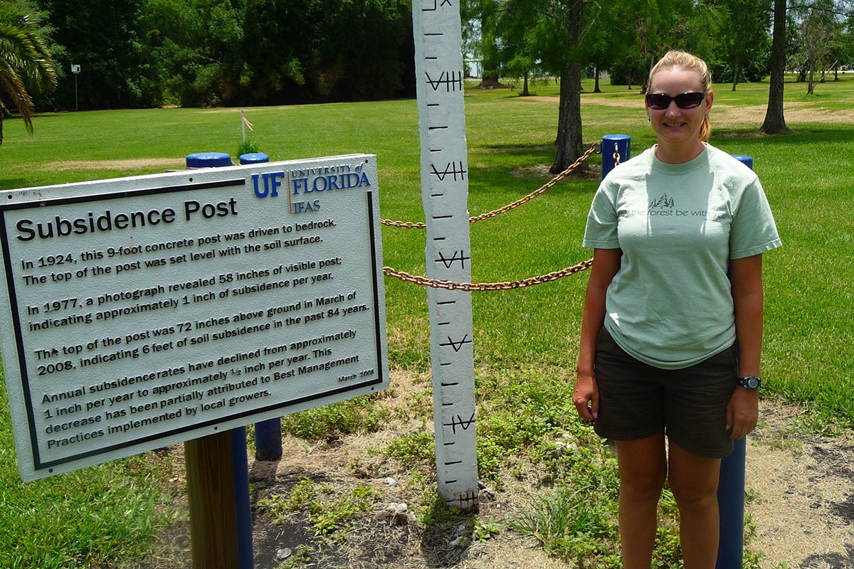Lisa Chambers stands next a subsidence post that marks the amount of soil subsidence that has occurred over the last 100 years. It's been about 6 feet of soil loss.