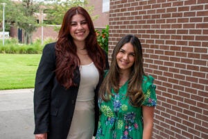 Paola Luigi and Susanna Beltran in front of a brick building with a shrub behind her