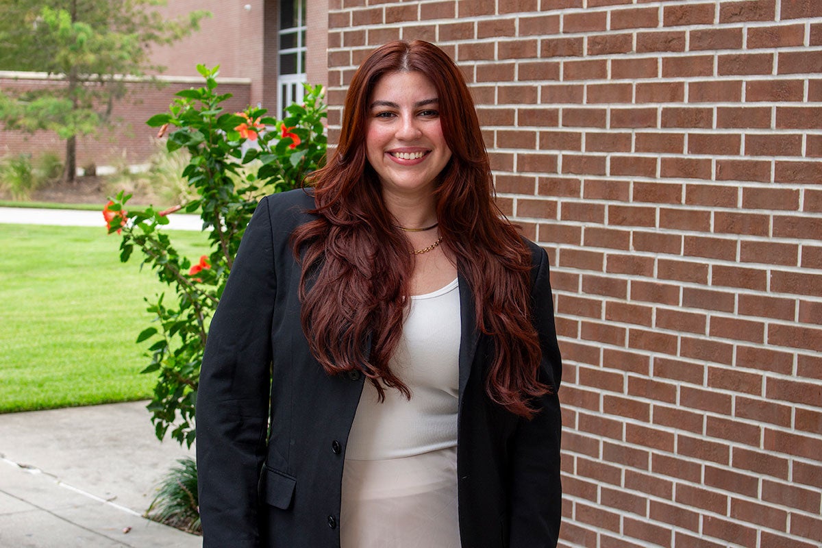 Paola Luigi in front of a brick building with a shrub behind her