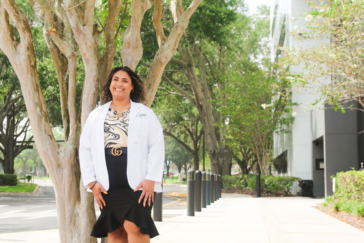 Aliyah Gonzalez wearing a white coat in front of the UCF College of Nursing building.