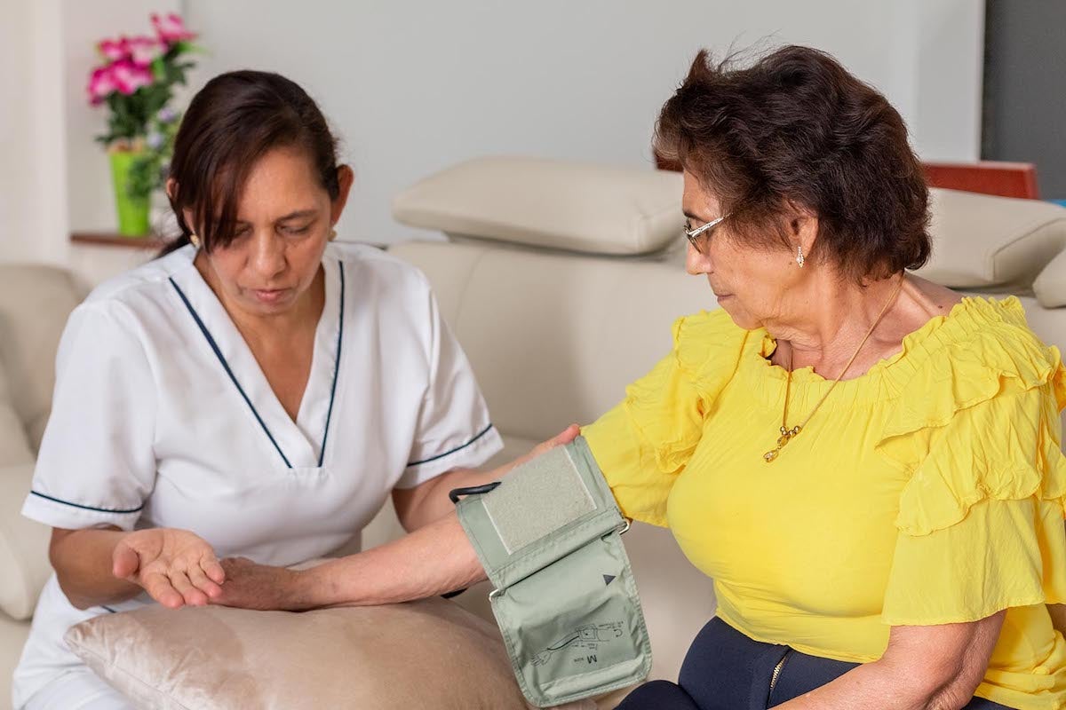 A nurse explains to an elderly woman how to use a digital blood pressure monitor.