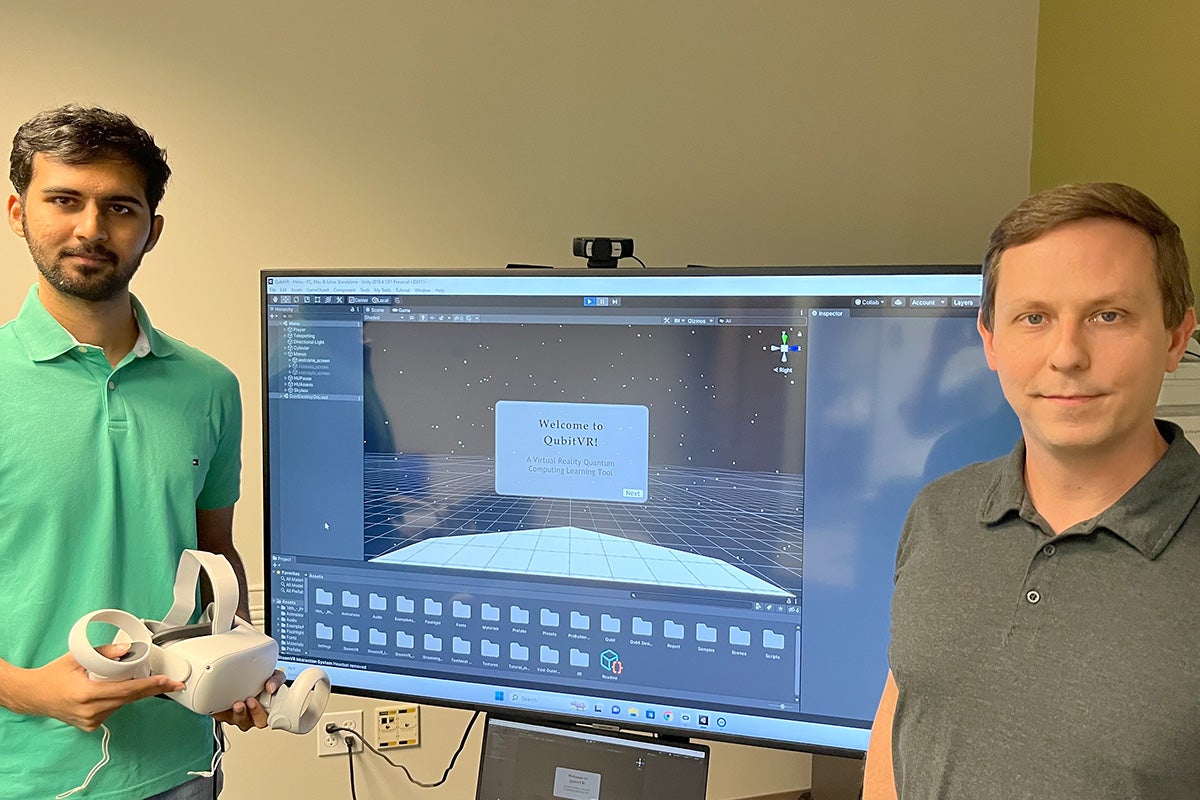 UCF Computer Science master’s student Keerthan Reddy Rajulapally and Computer Science associate professor Ryan McMahan stand in front of a monitor displaying the QubitVR application's start screen.