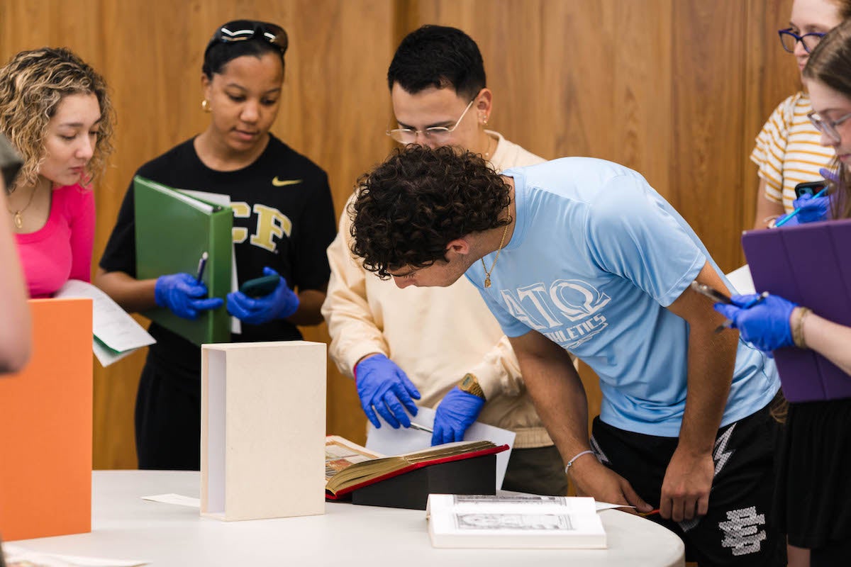 Six students surround and examine manuscript.