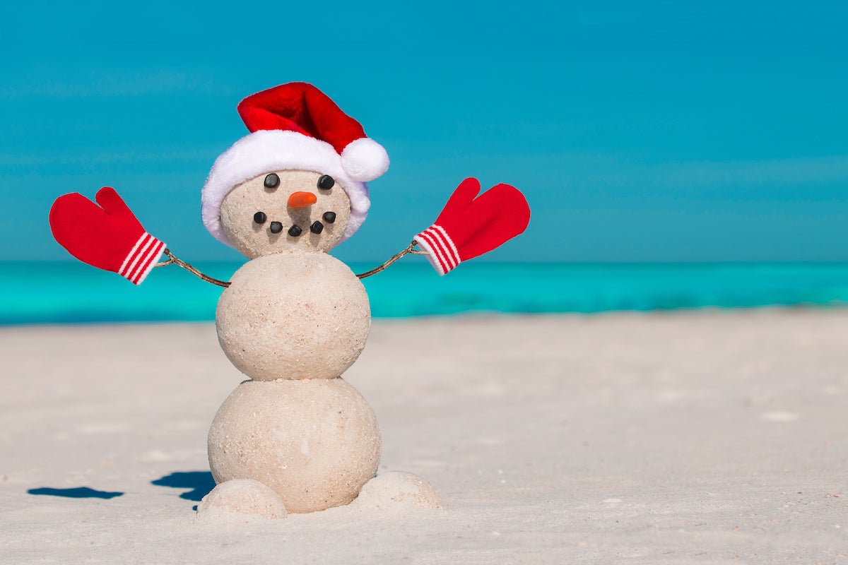 Sandy Christmas snowman in red Santa hat and mittens without sunglasses. Beach Snowman. Happy Smiley Snowman at sunny beach. Holiday concept for New Year post cards. Cold Florida Winter.