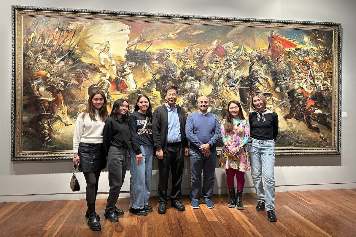 Naim Kapucu with students posing for a photo in front of a painting