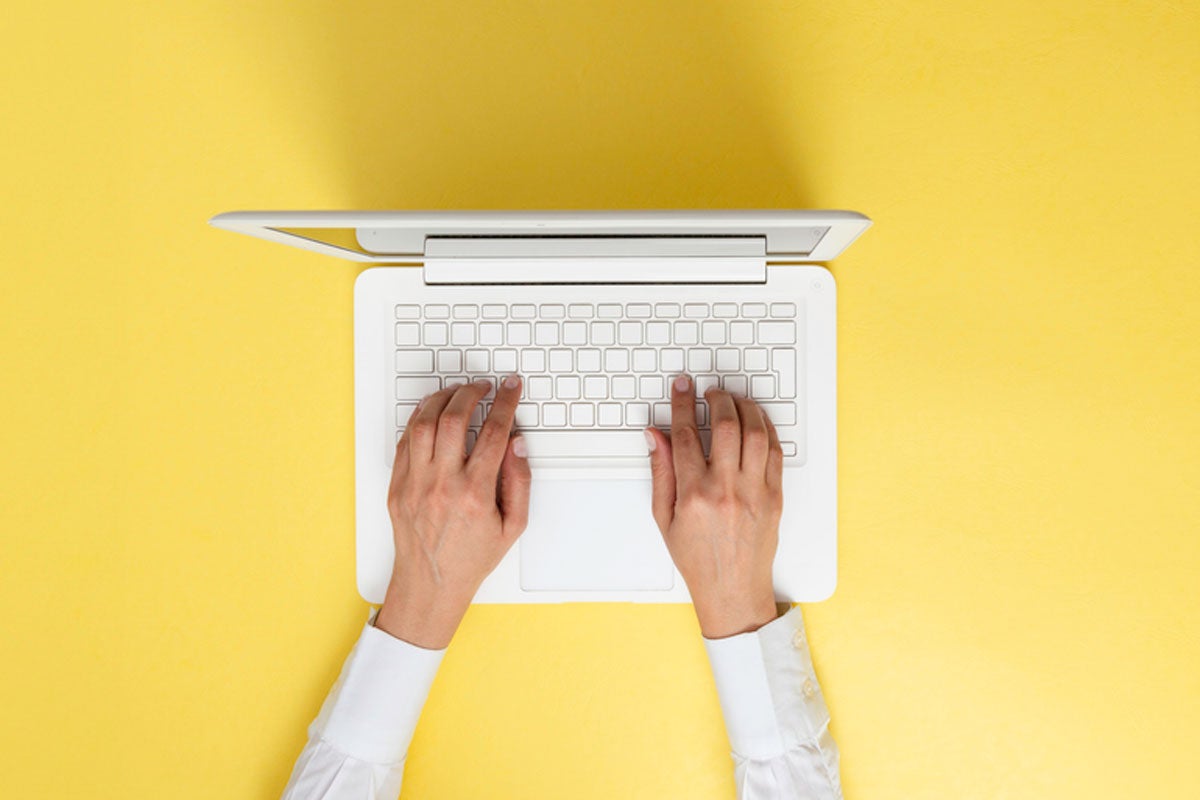 overhead view of someone typing on a laptop against a yellow background