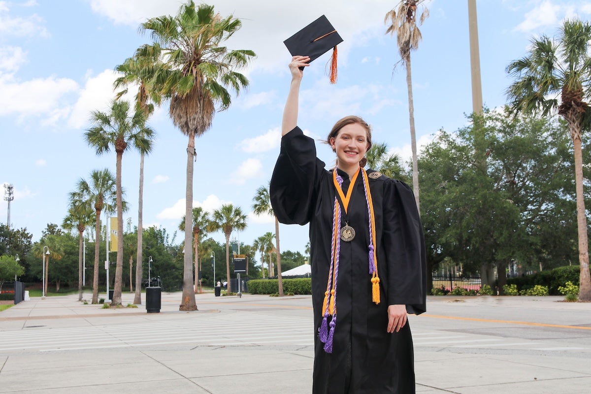 Rebekah May wearing a graduation gown while holding a graduation cap
