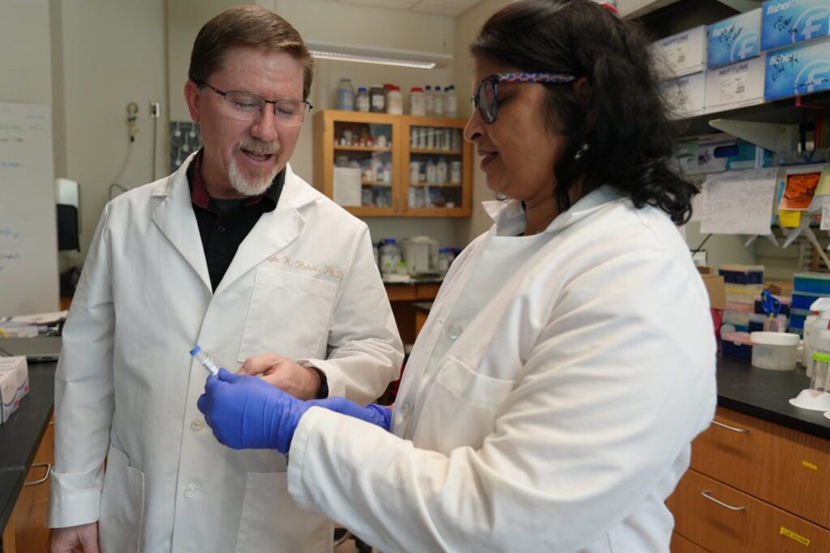 Two people wearing white coats and working in a lab