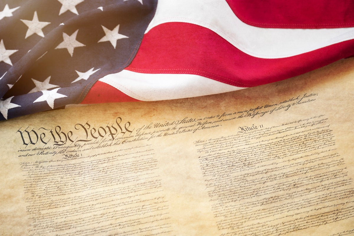 An American flag overlapping a copy of the Constitution