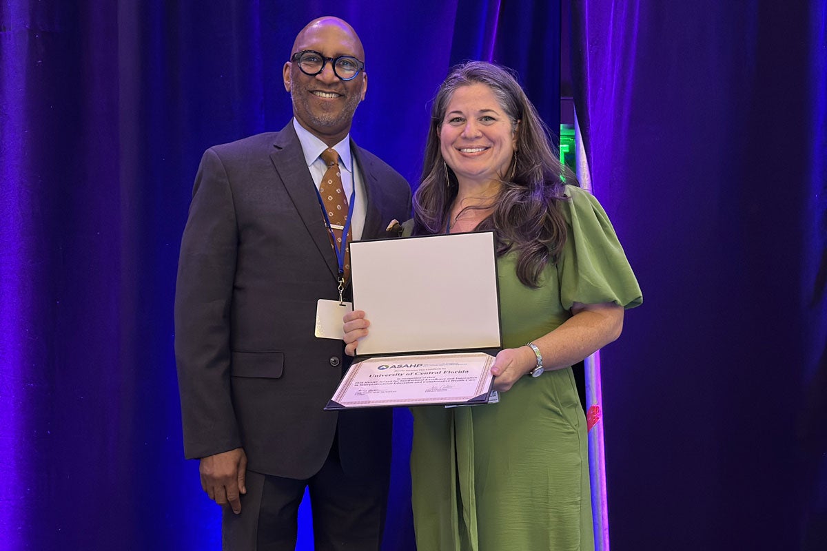 A man and a woman standing on a stage while she holds a certificate