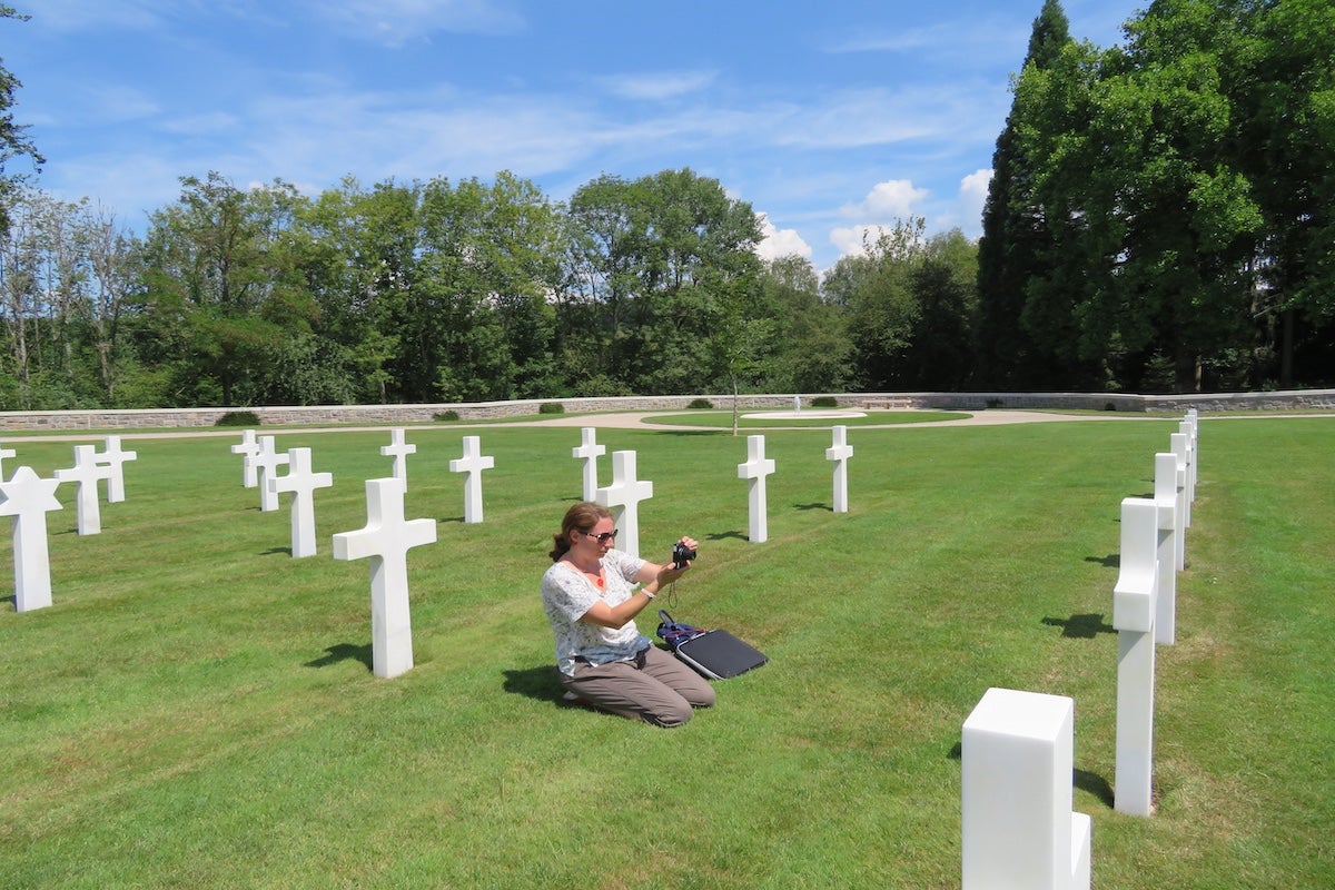 UCF Associate Professor Amelia Lyons kneels to take a photo of a burial site in the Epinal American Cemetery.