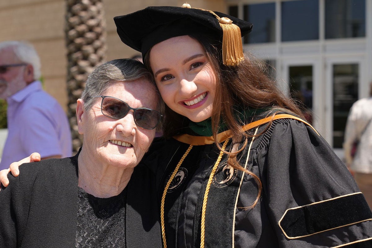 A graduate wearing regalia and posing for a photo with her grandmother