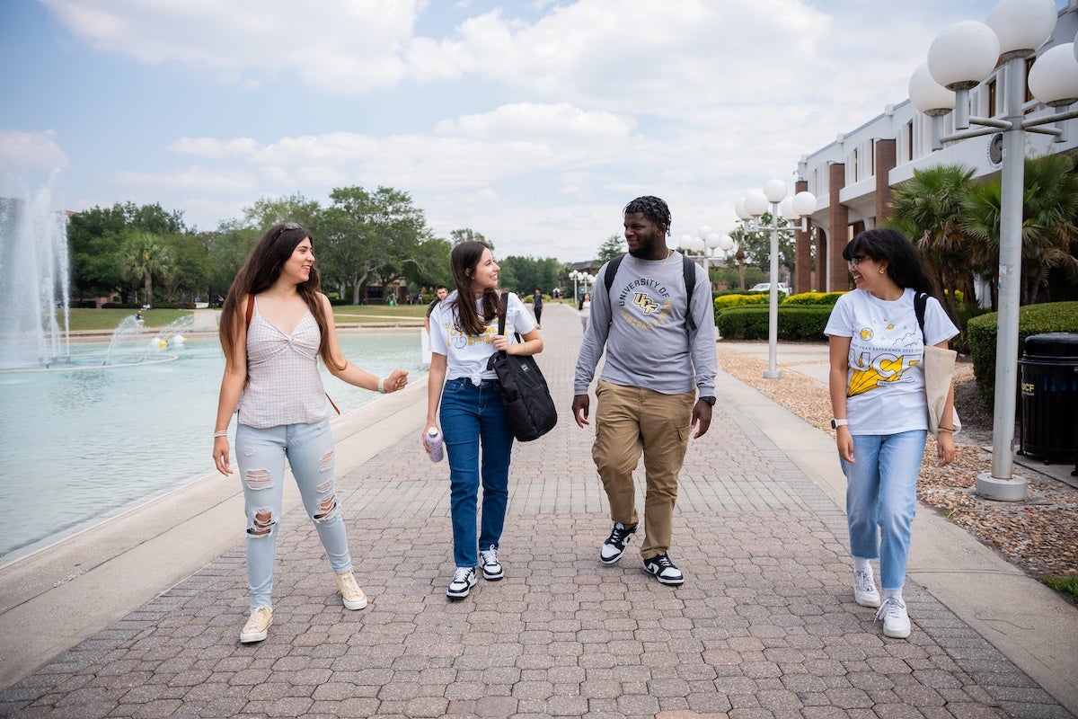 Four UCF students walk and talk together near the Reflecting Pond on campus.