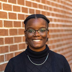 UCF biomedical sciences student Berline Civil stands smiling in front of a red brick wall.