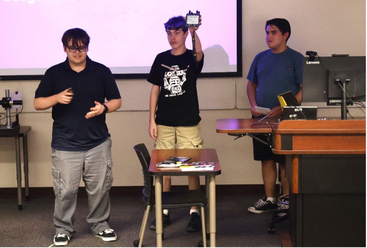 Students hold up electronics in front of audience.