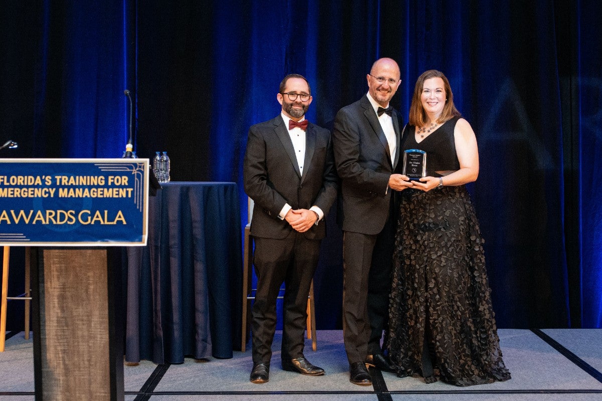 Claire Connolly Knox standing onstage holding the Campus Impact Award with gala presenters.