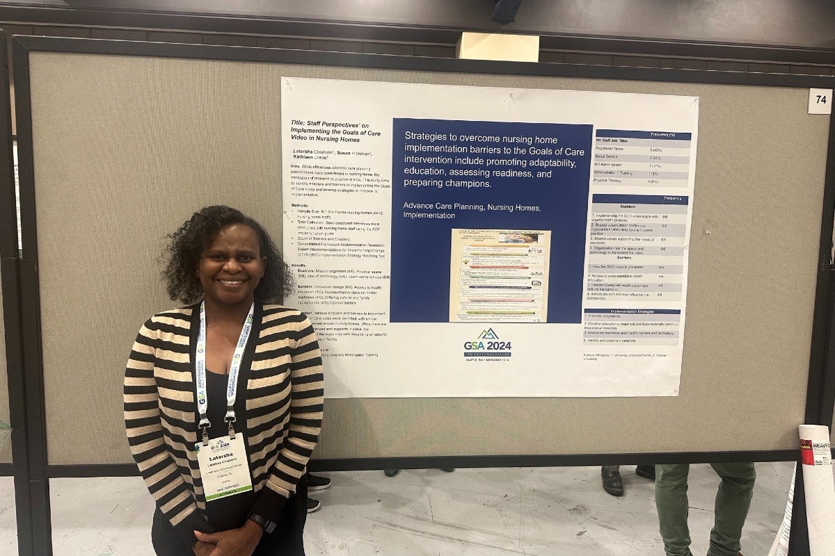 Latarsha Chisholm standing next to a poster of her research on advanced-care planning for nursing homes.