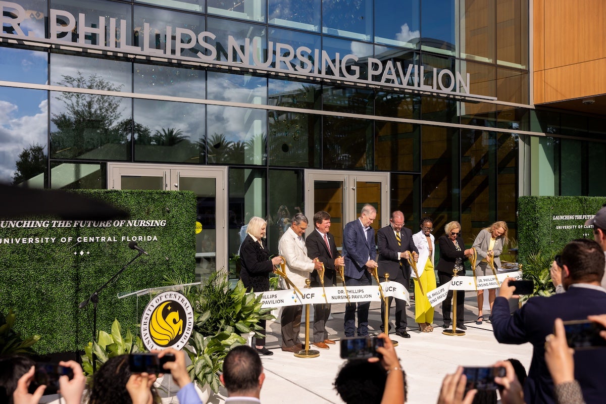A group of people cutting a ribbon in front of the Dr. Phillips Nursing Pavilion building at UCF’s Academic Health Sciences Campus in Lake Nona.