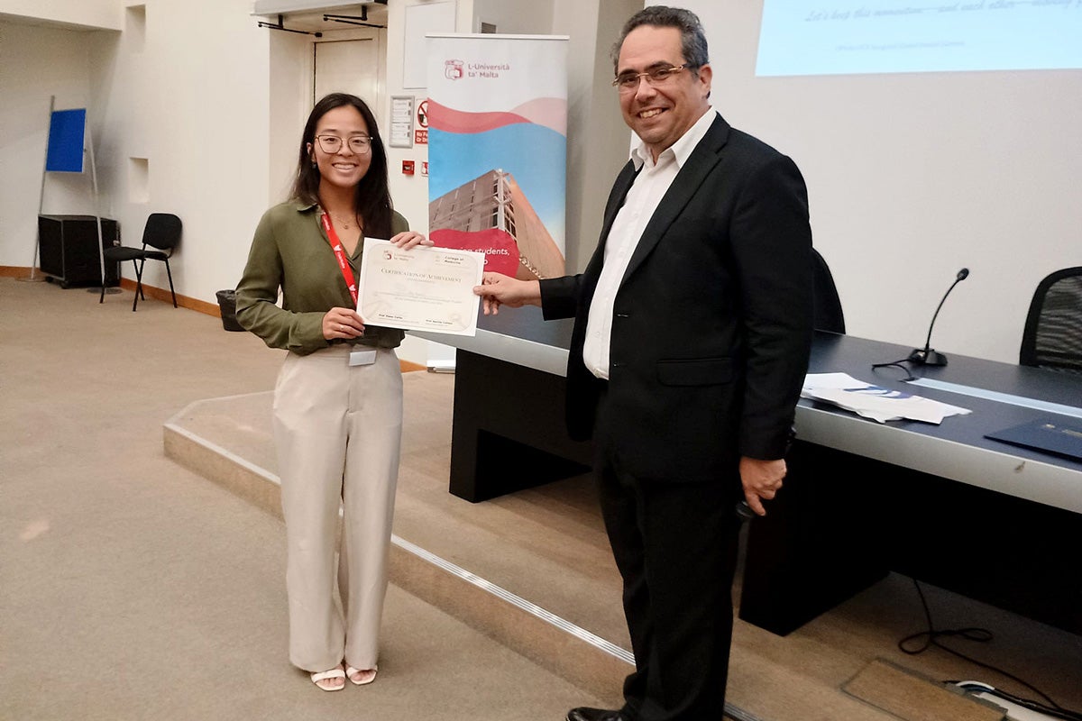Second-year med student Riley Nguyen receives a certificate of achievement for presenting her research at the global health summit from Dr. Neville Calleja, University of Malta professor of public health.
