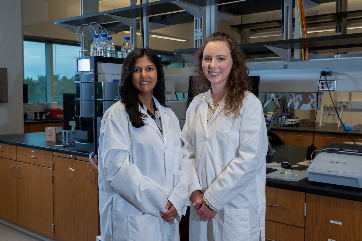 Two people wearing lab coats and standing in a lab