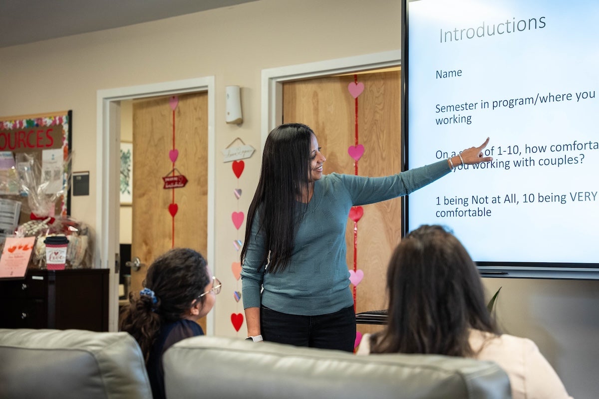 Sejal Barden standing at a presentation screen and pointing at a slide while her students listen.