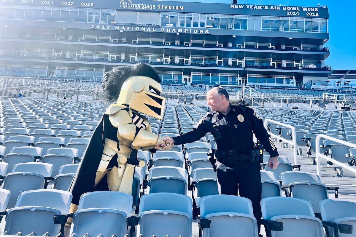 Carl Metzger, UCF’s associate vice president of public safety, shakes hands with Knightro while standing in the stands at FBC Mortgage Stadium.