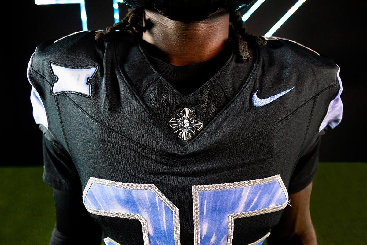 Close-up of black football jersey with silver number 25, blue Nike logo, and space-themed details on chest and shoulders.