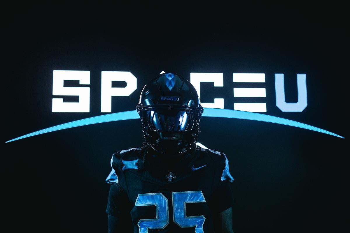 Football player in black uniform with number 25 stands under glowing “SPACEU” text and blue arc on dark background.