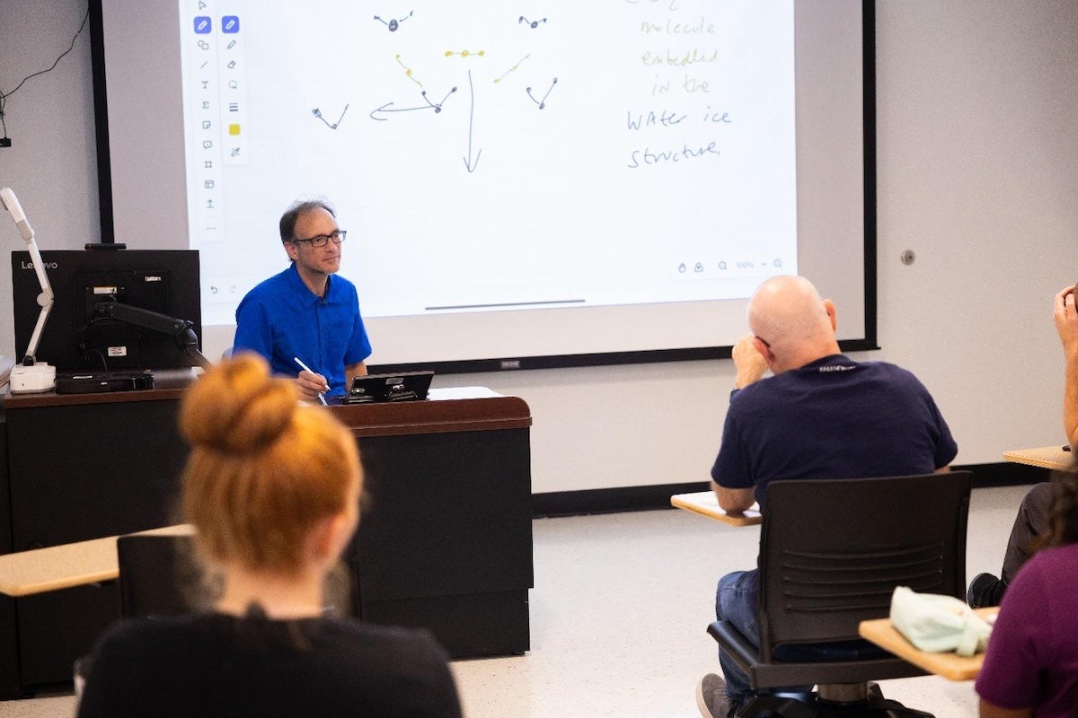 UCF Professor Yan Fernandez teaches a graduate course from the front of a classroom as students sit at desks.
