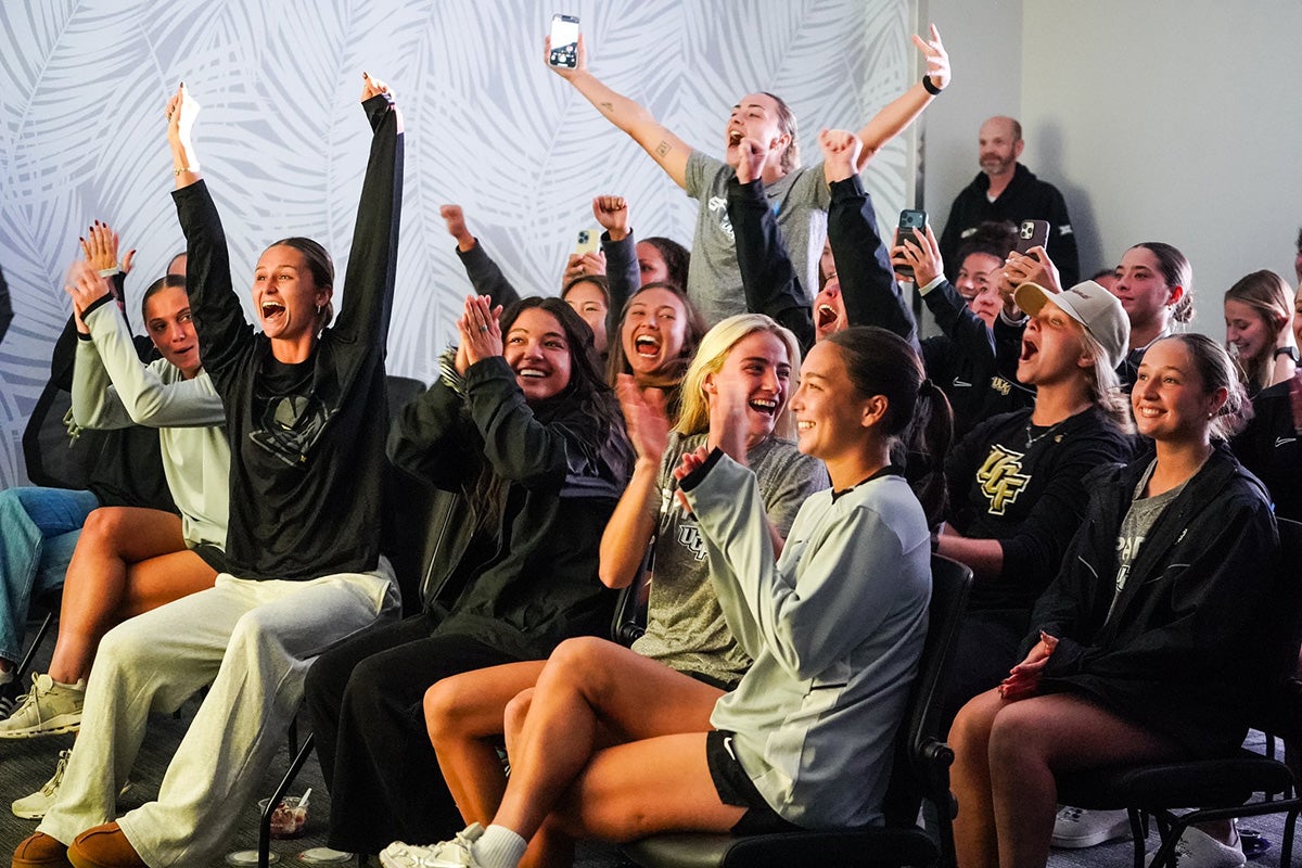 Group of women in black and gray shirts seated in room with gray and white palm-tree-designed walls