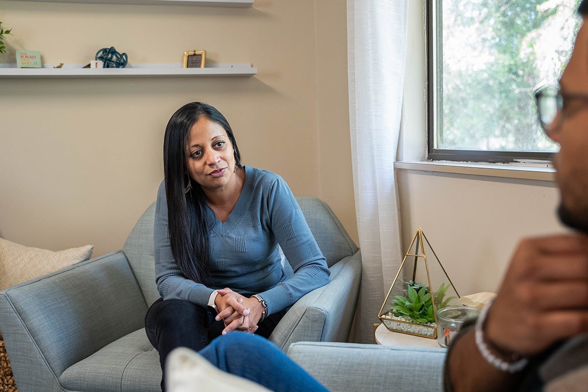 Sejal Barden, left, and a student sit across from each other in matching blue armchairs in a counseling room as they engage in conversation.