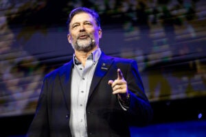 Man with graying beard wearing a gray buttondown shirt and dark suit speaks on stage