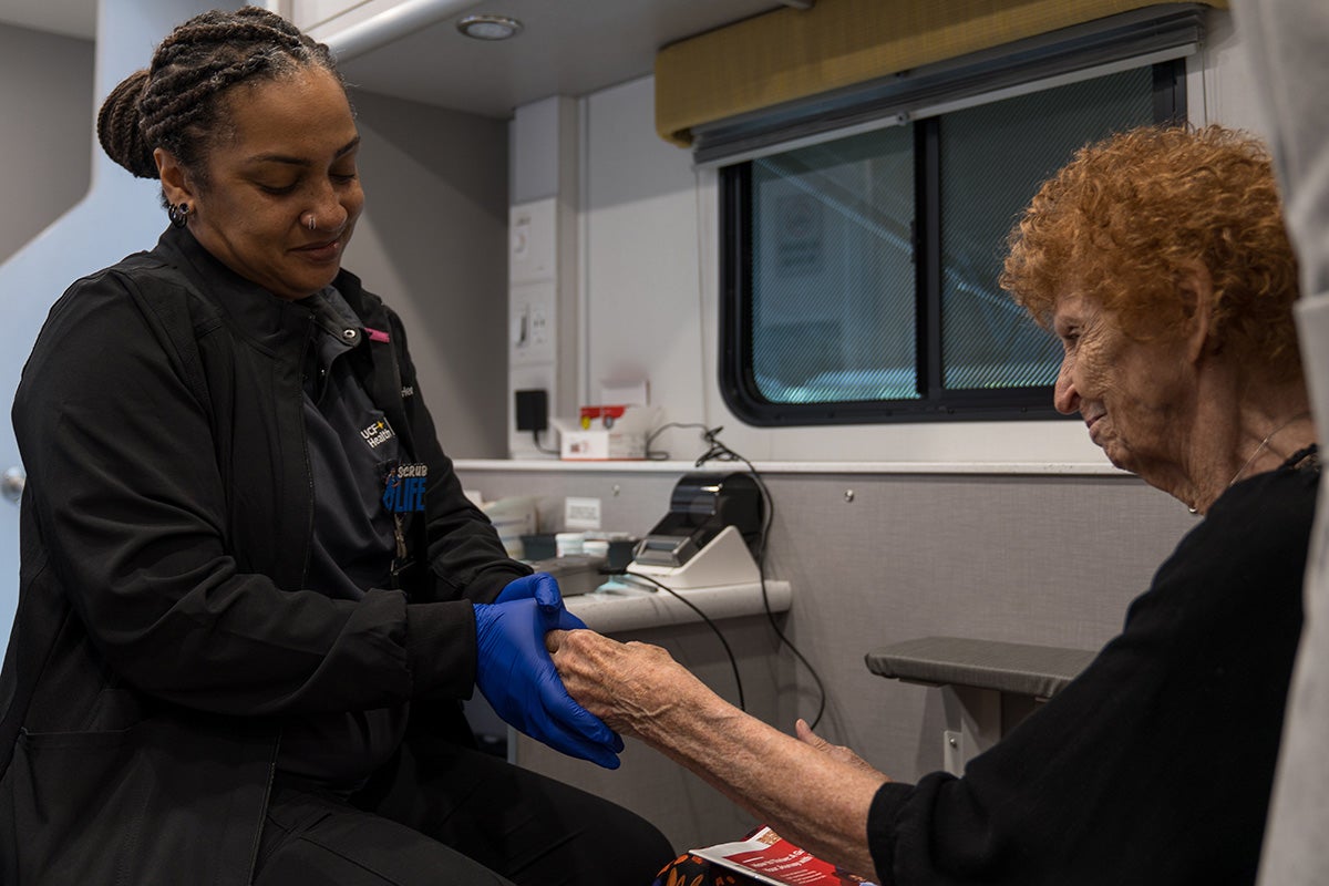 healthcare professional checks pulse of an elderly patient inside mobile health clinic