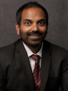Man in a dark suit, white collar shirt and red tie.