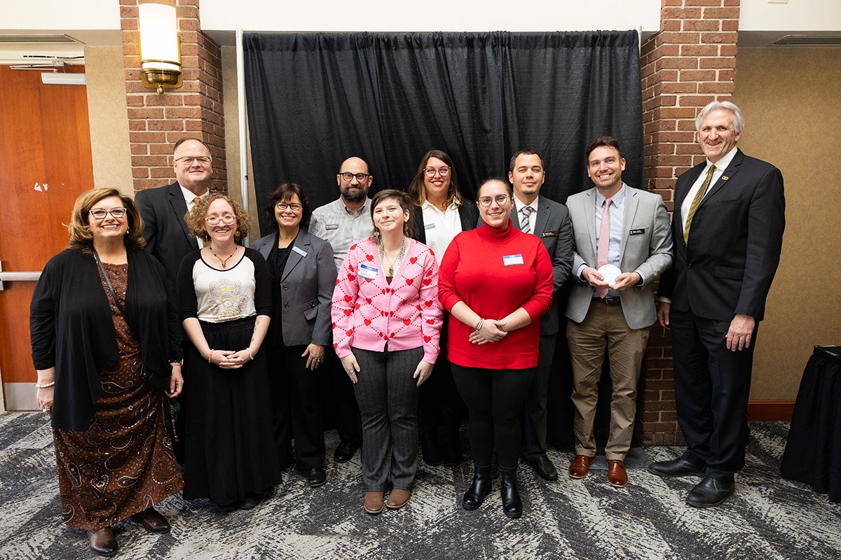 A group of faculty members in UCF's College of Arts and Humanities stands with Provost John Buckwalter in front of a black backdrop.