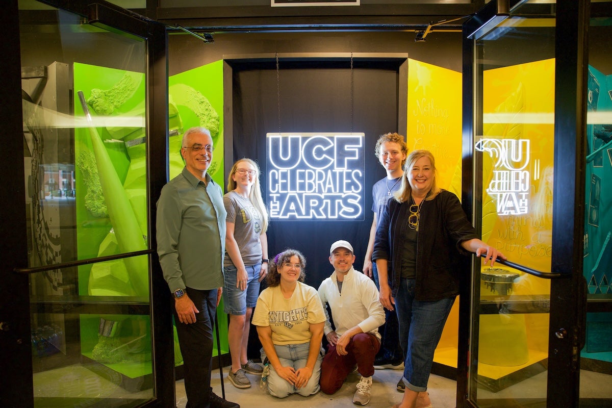 People posing for a photo in front of a neon UCF Celebrates the Arts sign