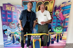 UCF art alum poses for a photo with his dad in front of a Teen Titans Go! promotional backdrop.