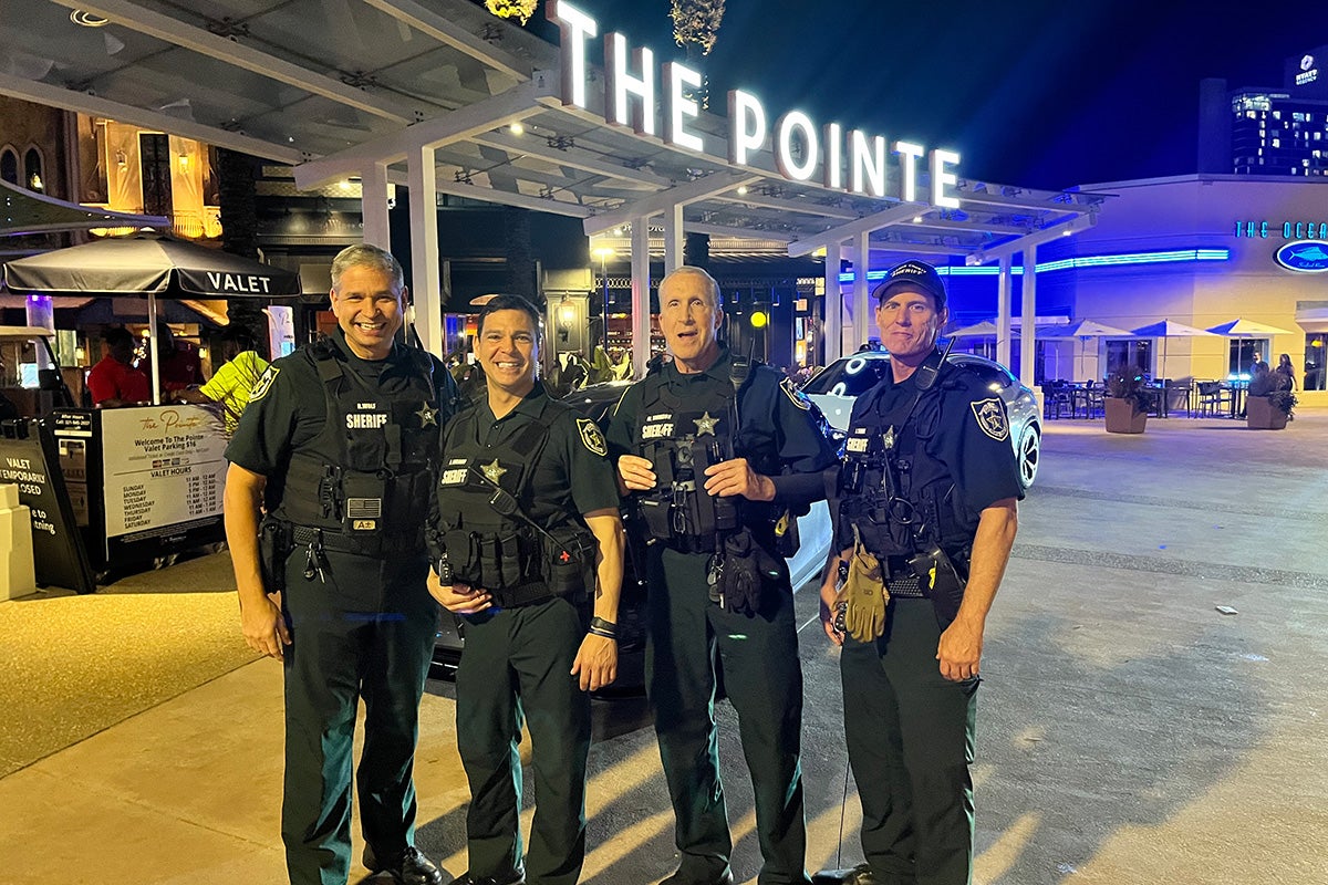 Four police officer pose in front of illuminated sign that reads The Pointe