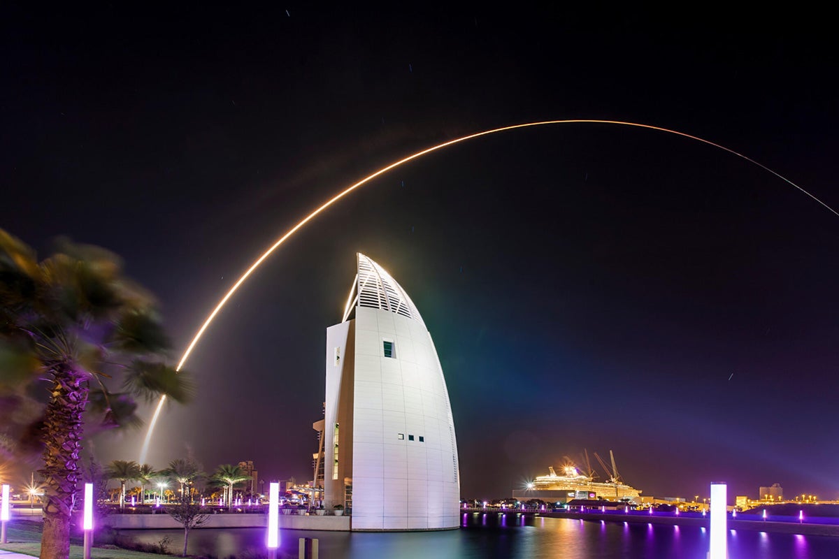 Rocket launch golden trail streaks across night sky at Port Canaveral cruise port