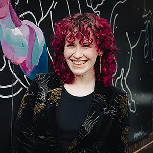 Portrait of woman with purple-tinted hair in front of mural on wall
