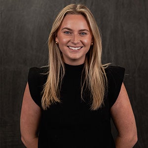 Portrait of smiling blonde woman in black top with arms behind her back