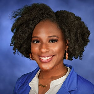 Portrait of smiling woman with black curly hair, parted to the side, in blue blazer