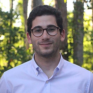 Portrait of man with glasses in white collar shirt, standing near trees outside
