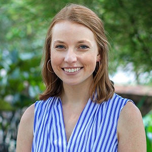 portrait of smiling woman in white and blue striped sleeveless blouse, standing outside