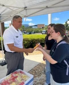 Ross Wolf hands popsicle to student under a white tailgate tent