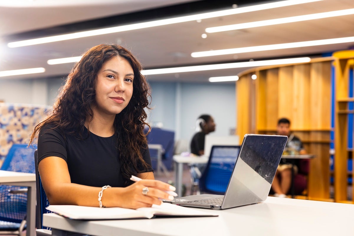 A UCF student studies at a table with an open laptop in front of her.
