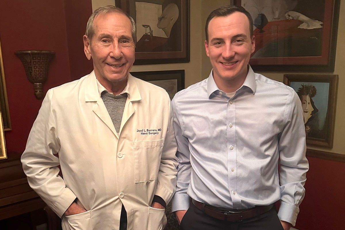 A man with gray hair wearing a white lab coat poses next to younger man in collar shirt