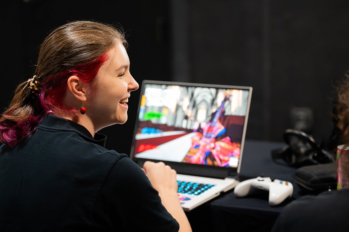 Young woman with a pony tail sits in front of open laptop with colorful graphics