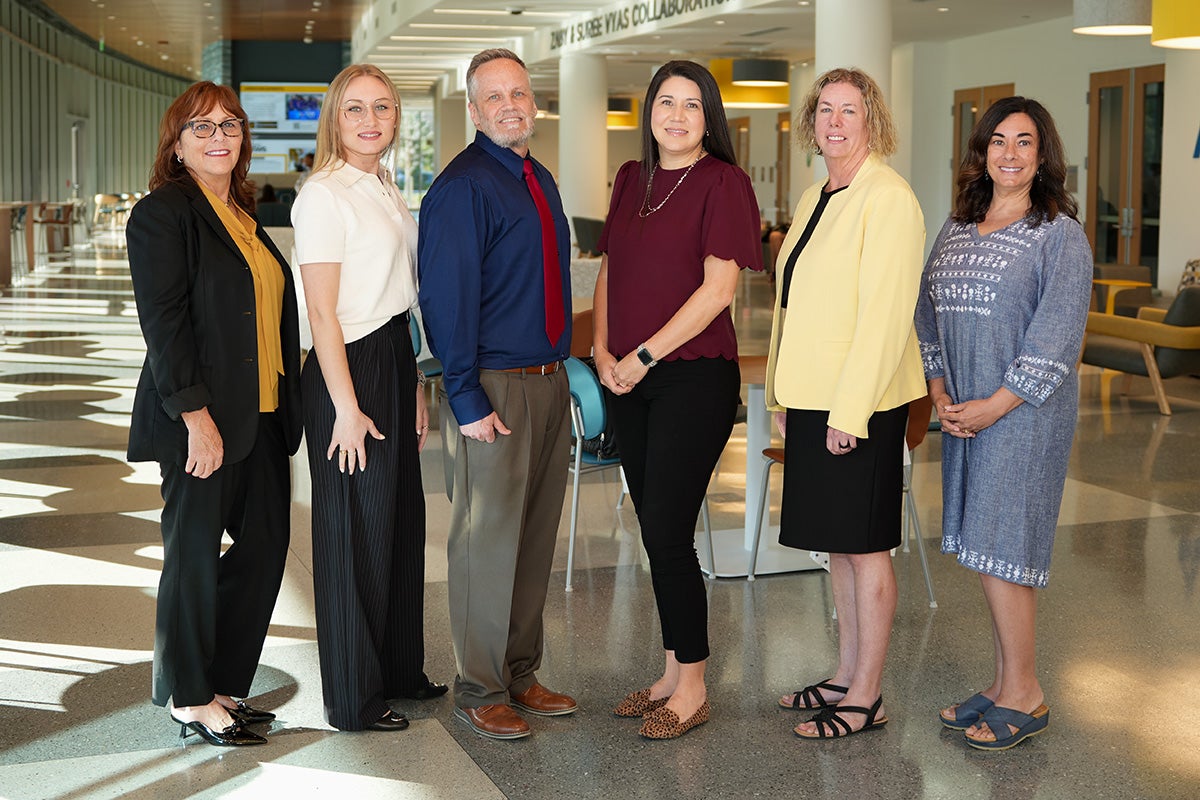 Six faculty members from College of Nursing pose in v formation in lobby of building