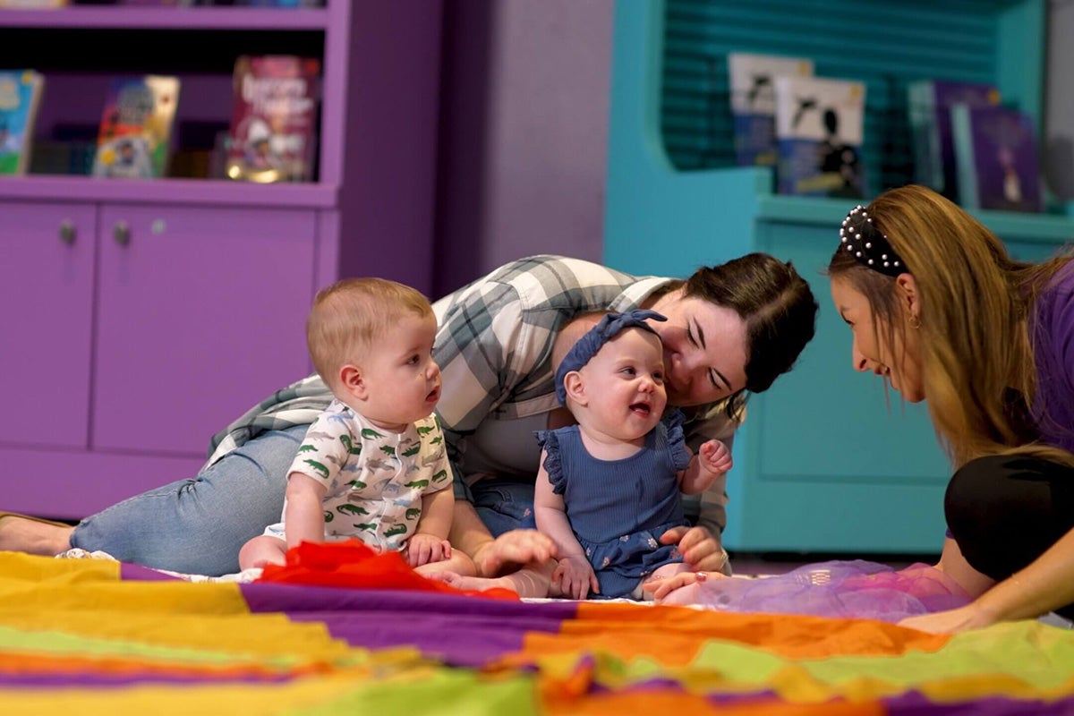 two babies smile at woman leaning down to interact with them